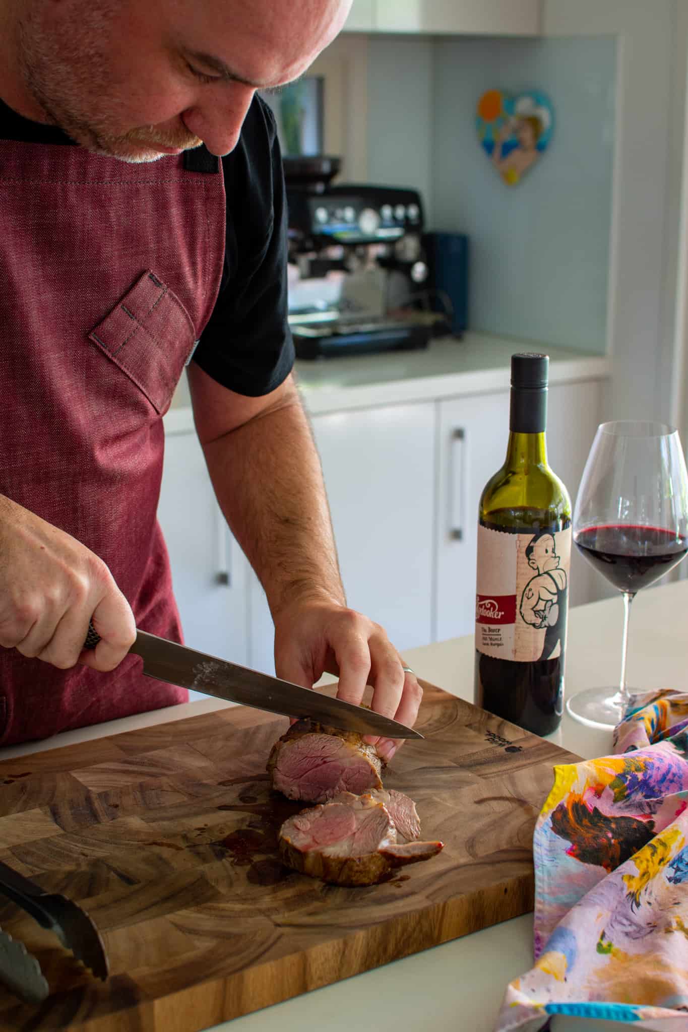 someone slicing mini roasted lanb shoulder with wine next to the chopping board