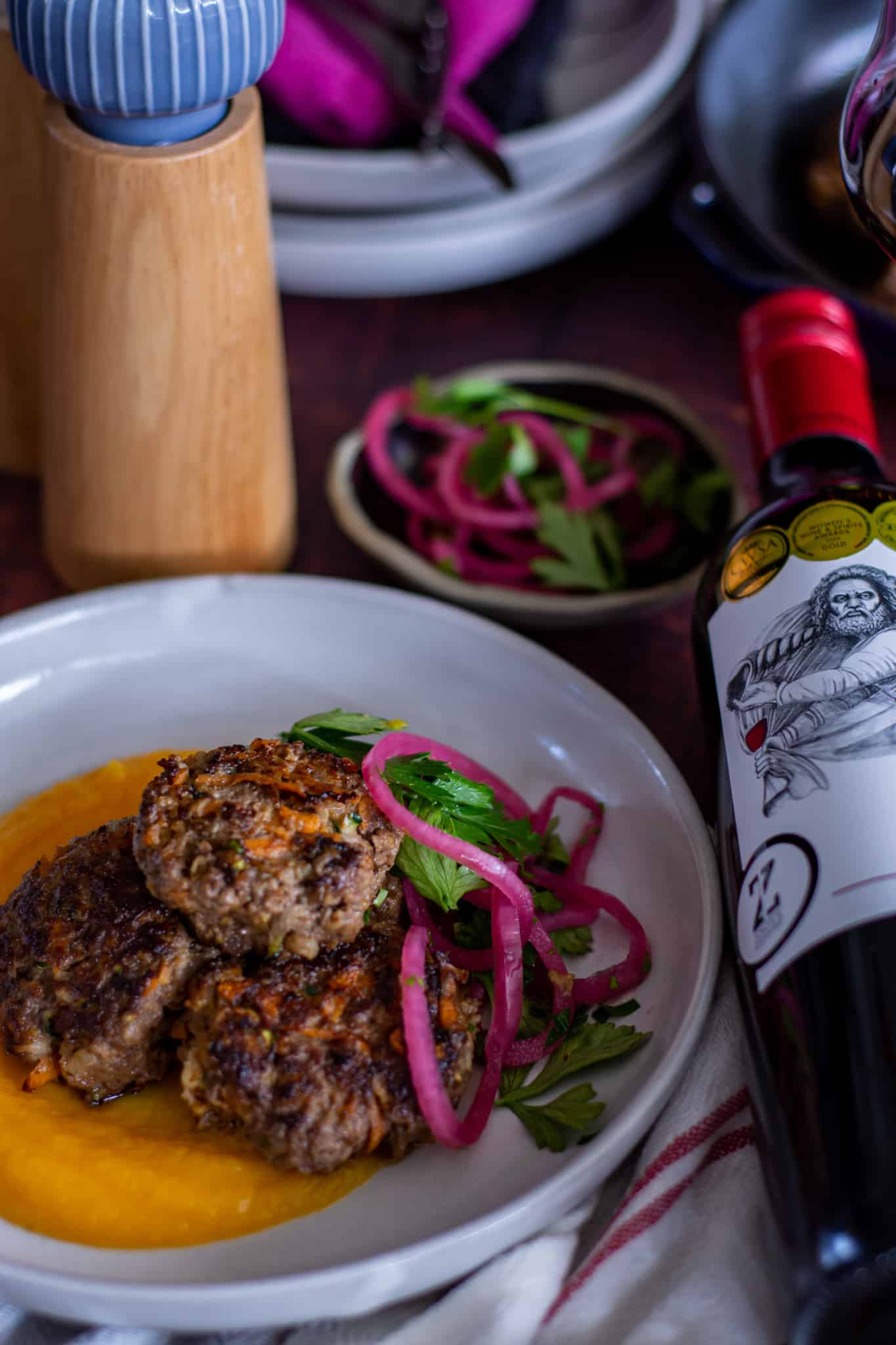 close up of beef rissoles on a plate with a bottle of wine next to plate