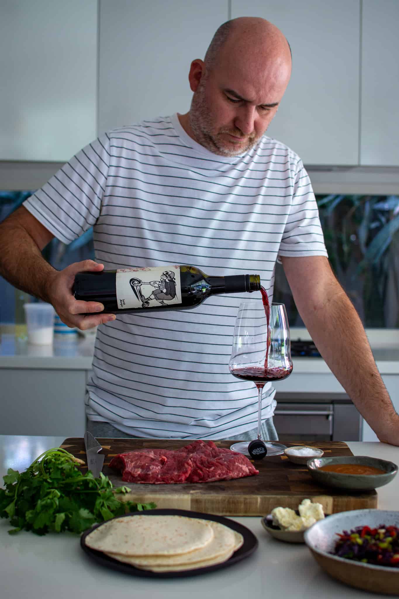 Someone pouring Mollydooker wine in the kitchen with food on the counter