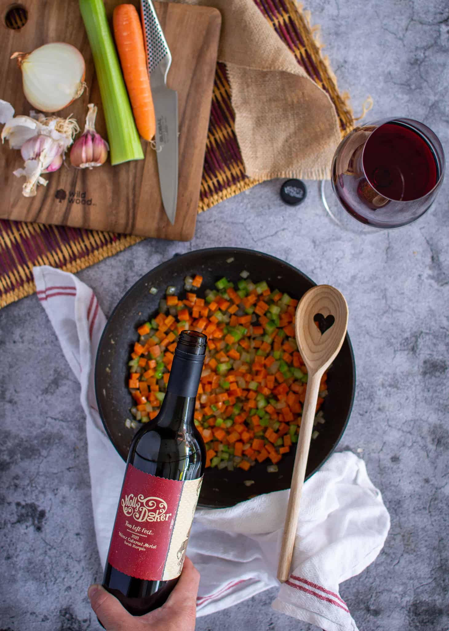 wine being poured into large saucepan full of vegetables
