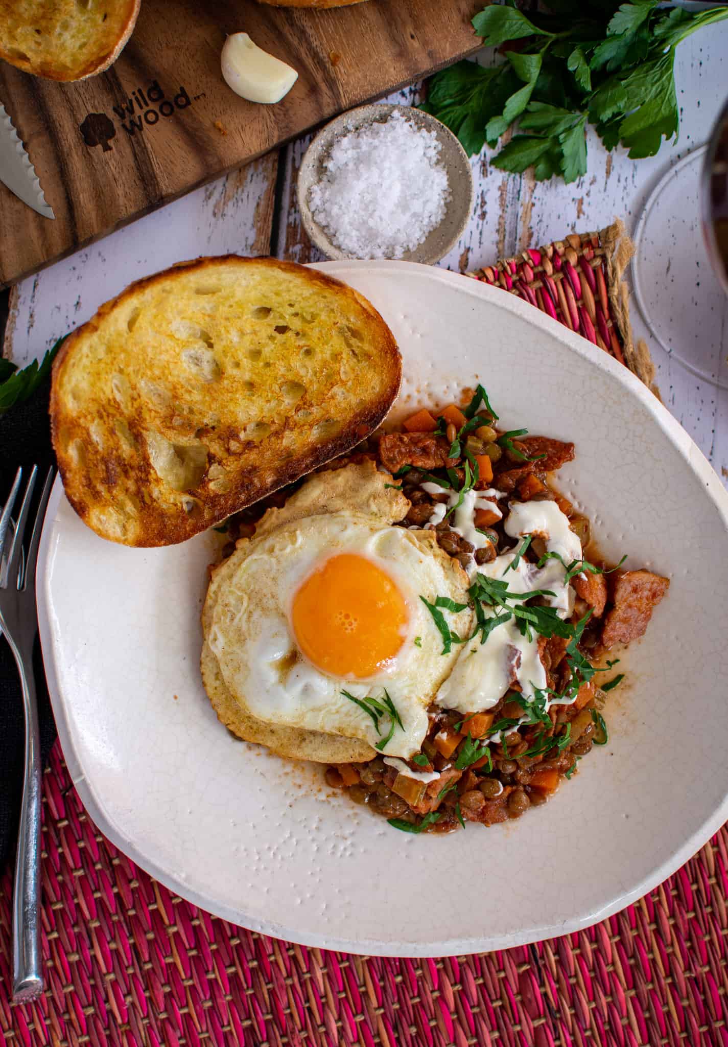 a birdseye view of bacon lentil stew on a white plate with grilled bread beside it
